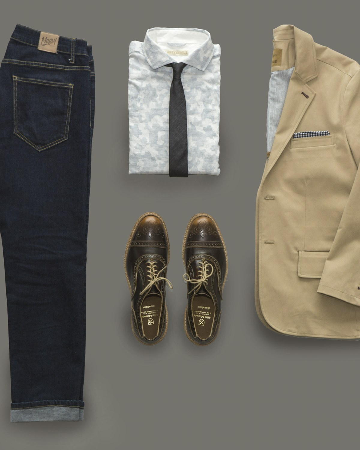 Dark denim jeans with a white shirt, tie, tan blazer and brown brogues, flat lay