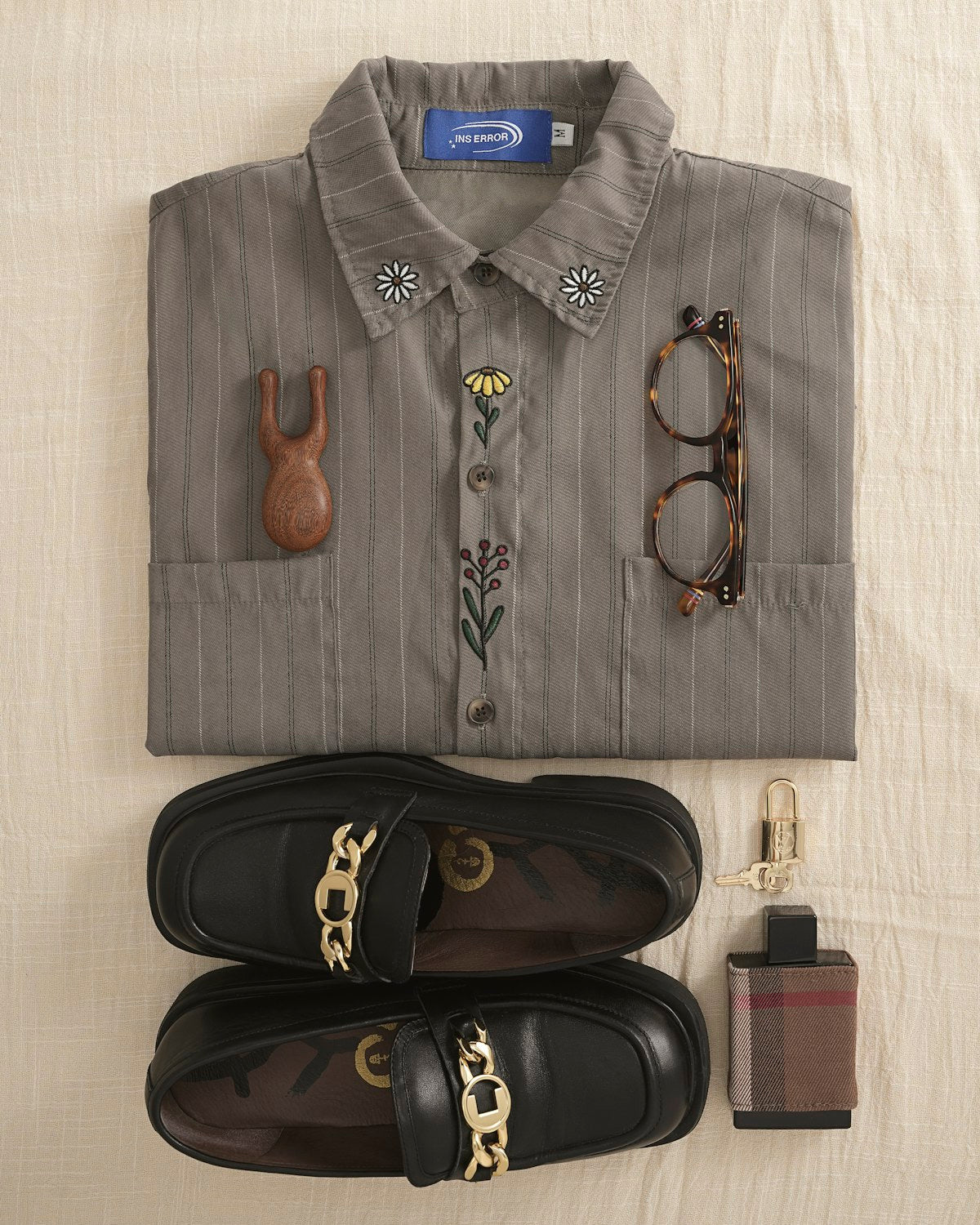 Folded grey shirt with loafers, glasses and a fragrance bottle, flat lay