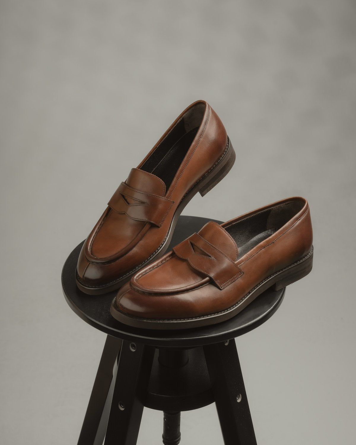 A pair of brown leather penny loafers resting on a dark wooden stool
